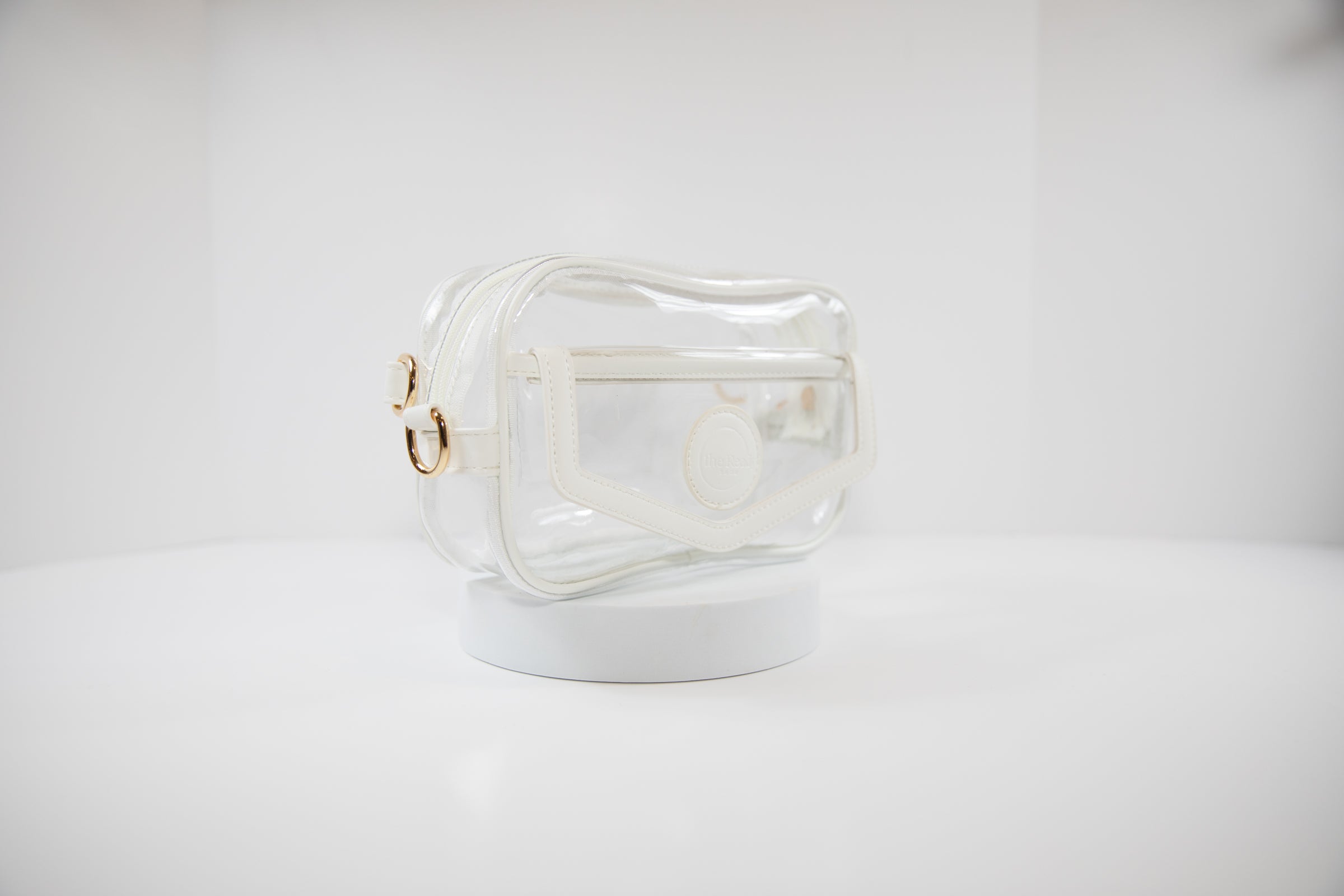 Clear Stadium Bag with gold hardware, side facing, that can be worn as a crossbody or body bag.