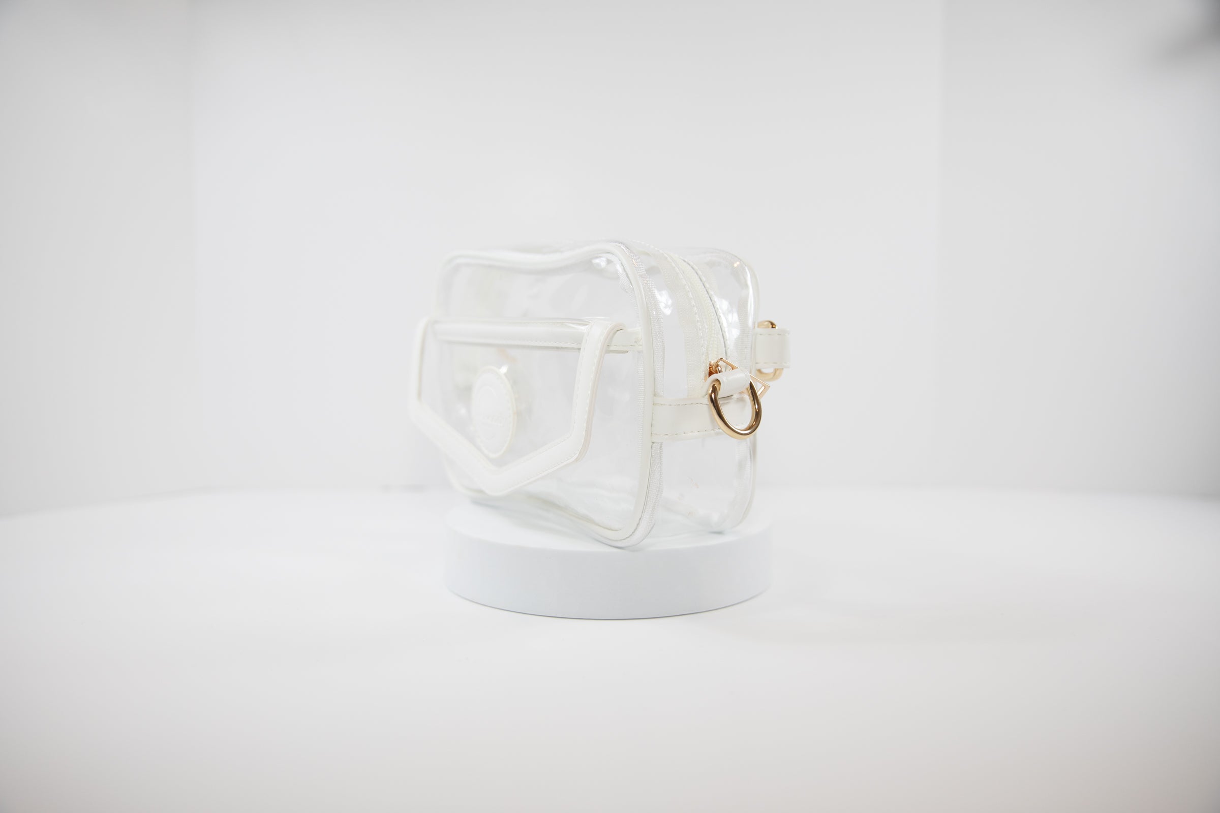 Clear Stadium Bag with gold hardware, side facing, that can be worn as a crossbody or body bag.